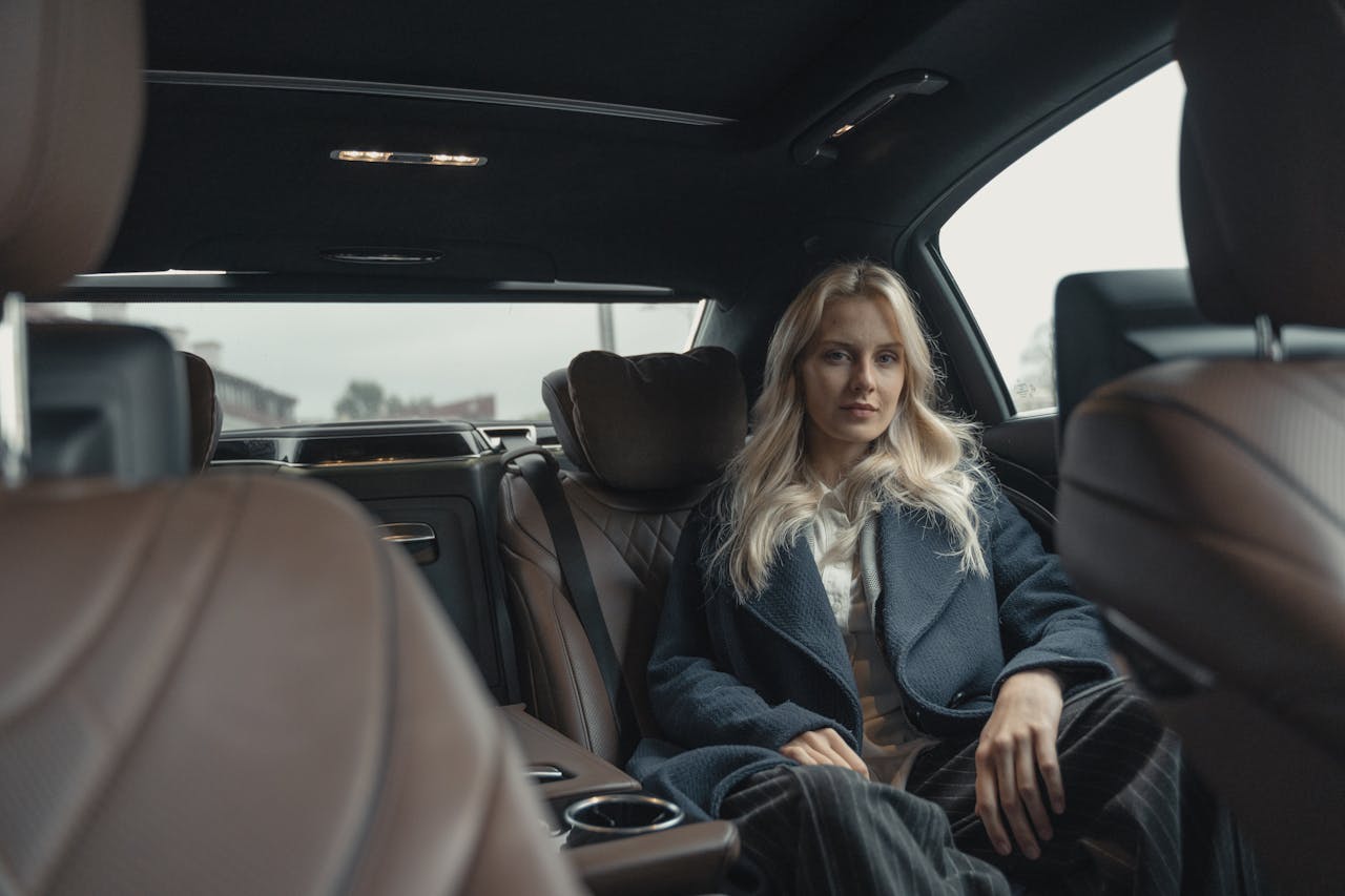 Elegant woman in a blue coat sitting in the back seat of a luxury car.